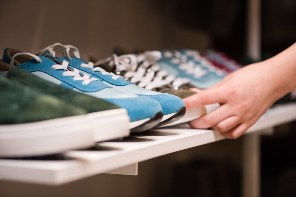 Close-up of female hands putting sneakers suede shoes collection on store rack. Consultant arrange colorful new shoes for sale at boutique mall.