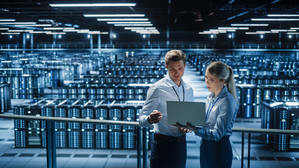 Data Center Female e-Business Enrepreneur and Male IT Specialist talk, Use Laptop. Two Information Technology Professionals on Bridge Overlooking Big Cloud Computing Server Farm